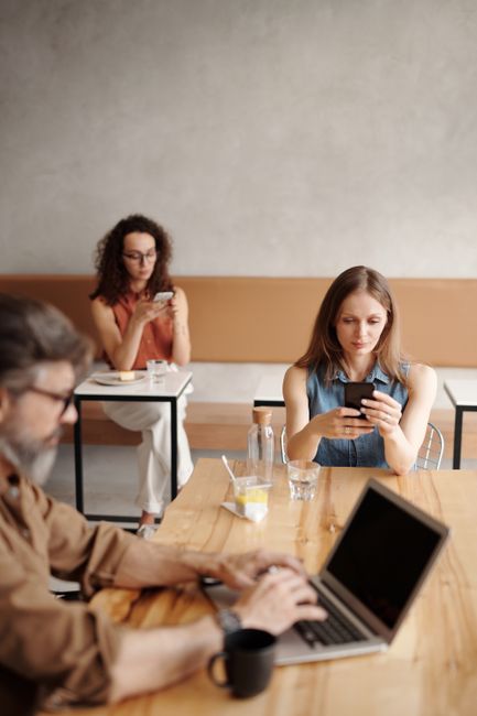Adults engaging with phones and laptop in a modern coffee shop setting.