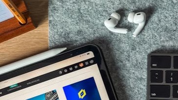 A top view of a sleek workspace featuring an iPad, AirPods, and keyboard on a felt surface.